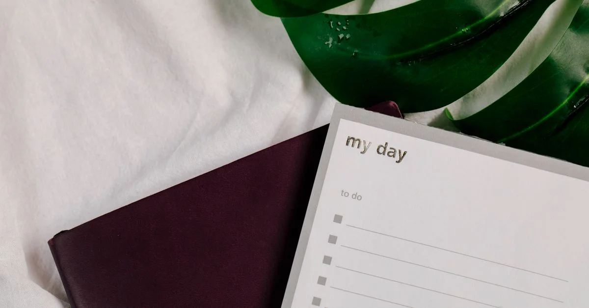 Un gros plan d'un carnet de liste de tâches avec de feuilles vertes luxuriantes sur une surface textile blanche.
