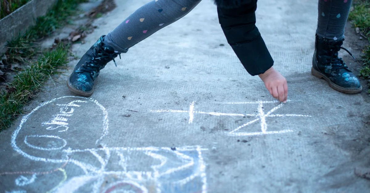 Un enfant dessine à la craie sur un trottoir, créant un art de rue ludique dans un cadre extérieur.