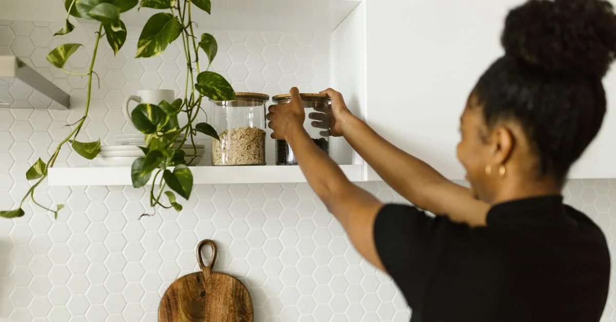 Femme organisant des denrées sèches sur des étagères de cuisine, mettant l'accent sur l'organisation et un design épuré.