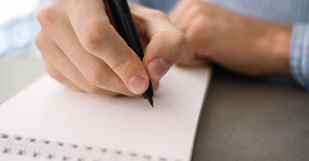Image détaillée d'une main écrivant avec un stylo sur un carnet à spirales, se concentrant sur les tâches quotidiennes.