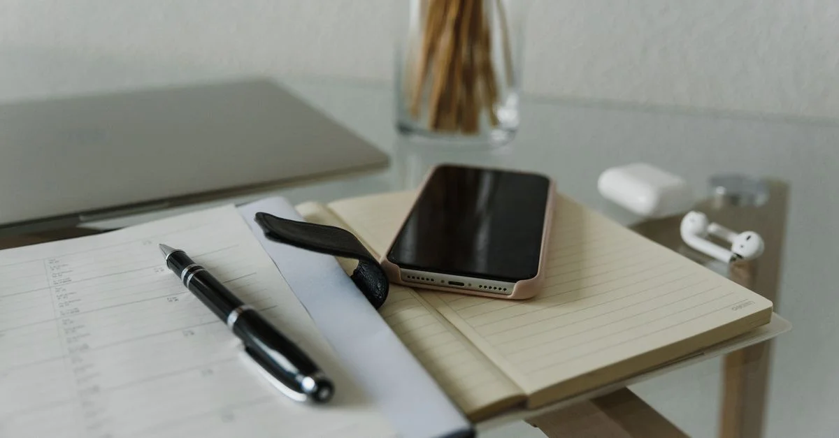 Un bureau minimaliste avec un smartphone, un carnet et des écouteurs sans fil pour un environnement de travail moderne et productif.