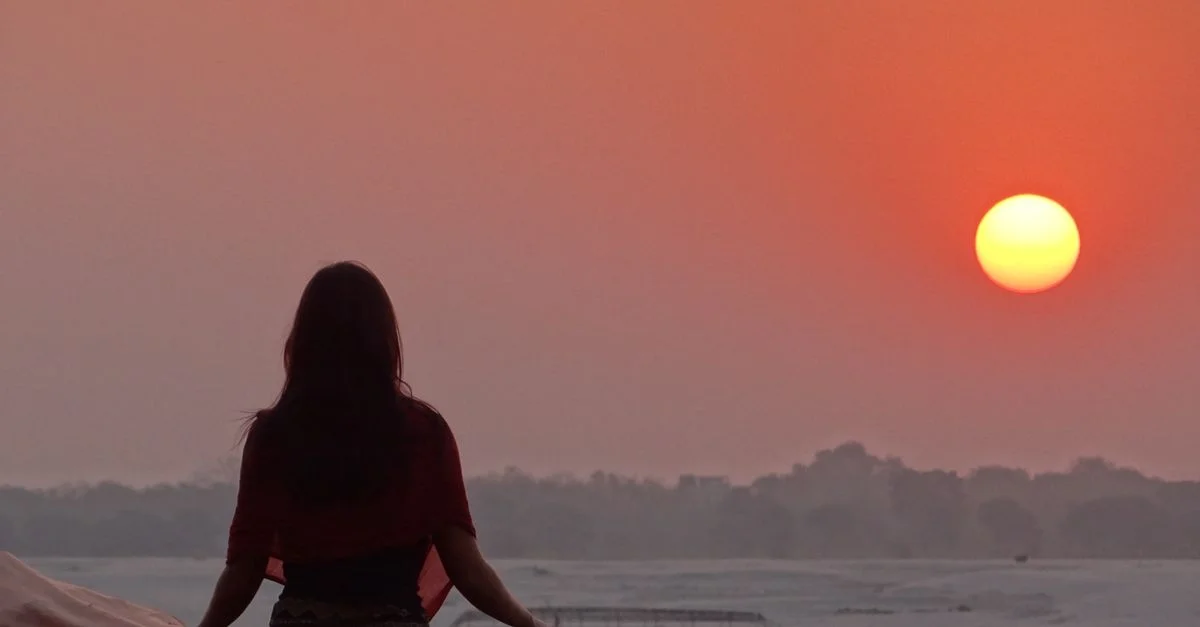 Scène sereine d'une femme méditant au coucher du soleil près du fleuve Gange à Varanasi, Inde.