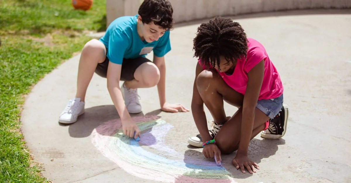 Deux enfants dessinant avec des craies colorées par une journée ensoleillée au parc.